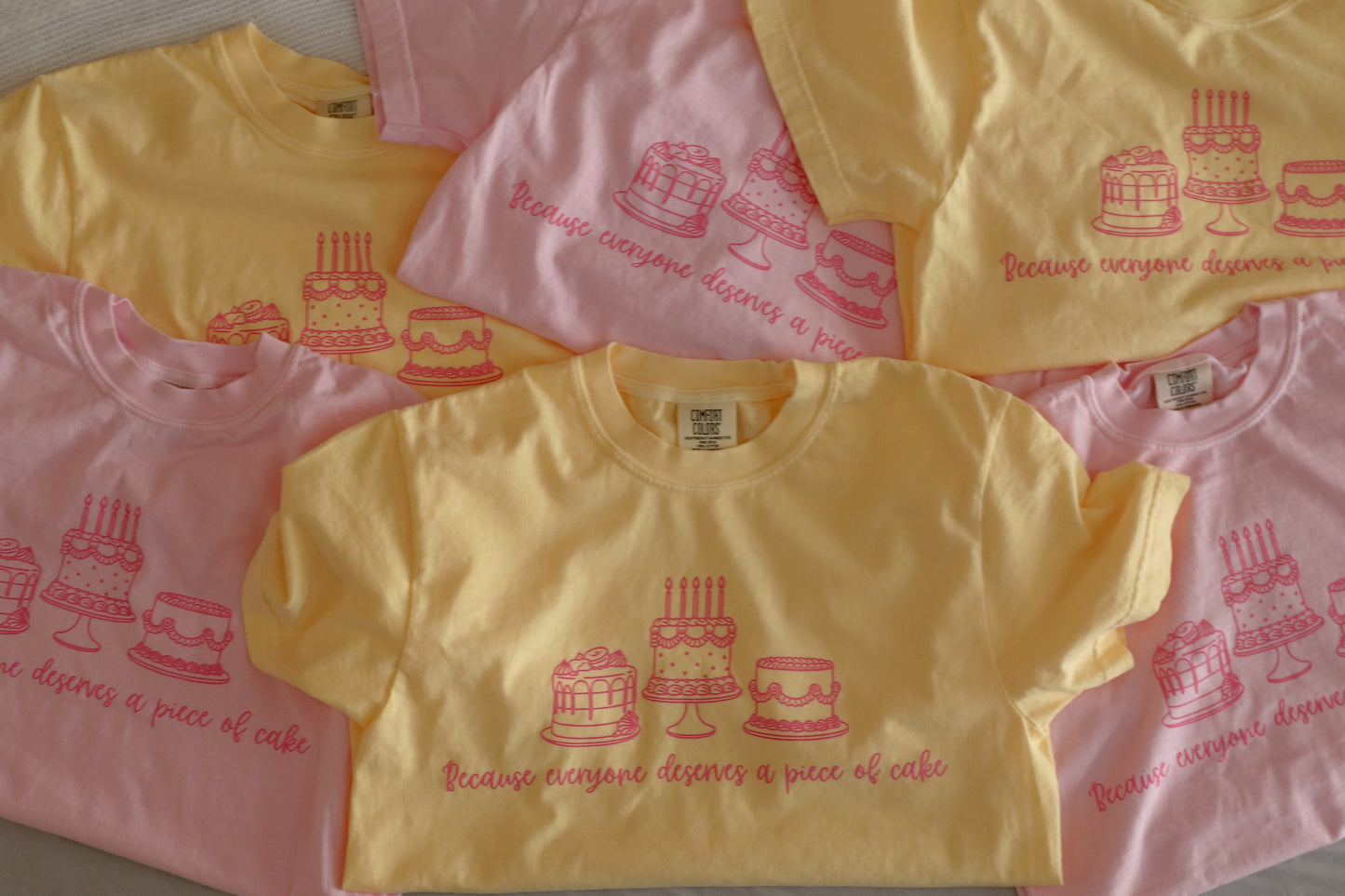 Yellow and pink shirts with cake design and text "Because everyone deserves a piece of cake"
